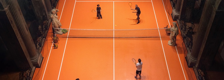 People playing on an orange tennis court in a church.