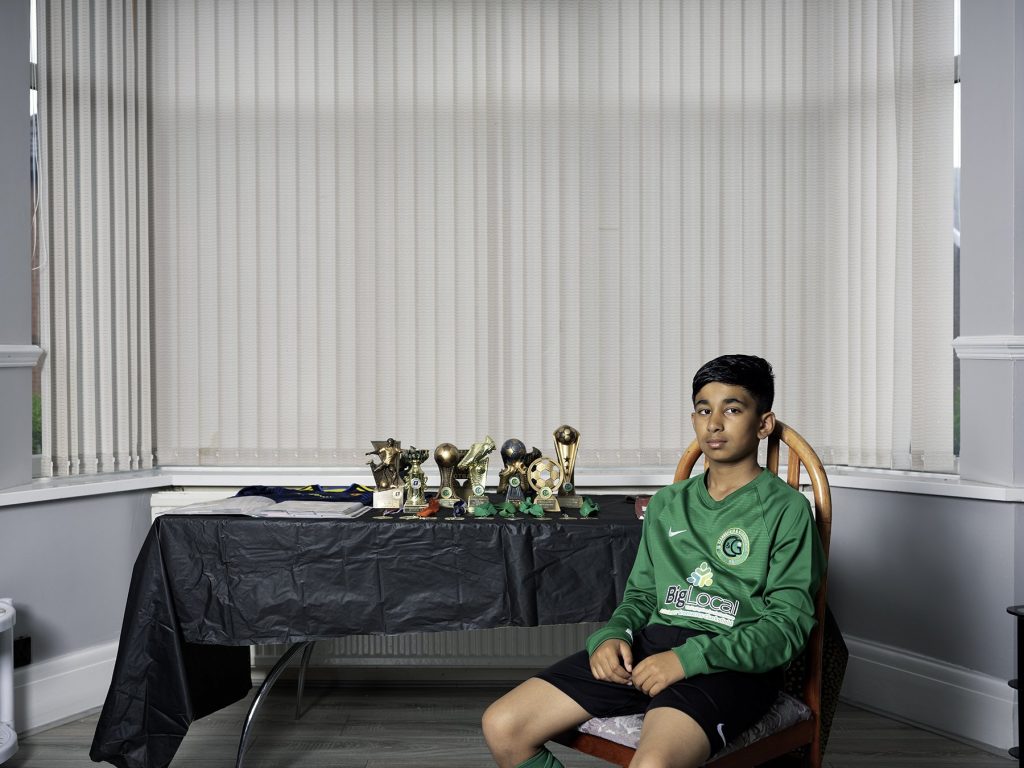 A boy sitting with his football trophies
